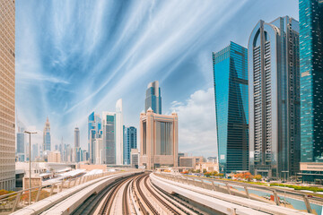 Fototapeta na wymiar Metro road among glass skyscrapers in Dubai. Metropolitan railway among modern glass skyscrapers in Dubai. Traffic on street in Dubai. Urban background.