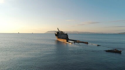 View of a old sunken ship on a shoal in sea against the sunset sky and mountains. Shot. Old...