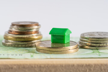 Small house between stacks of coins representing housing economy and house loan costs and interests.