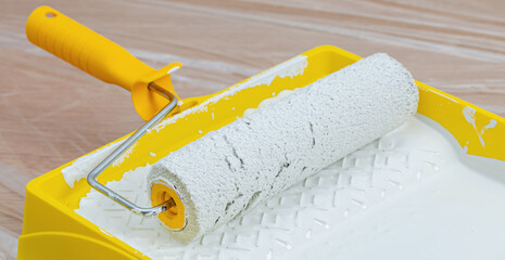 Paint roller in paint tray with white color. Repair and painting in the house. Construction and painting works.