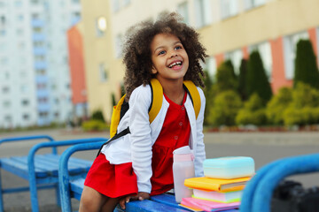 Cute Black schoolgirl eating lunch outdoors next the school. Healthy school breakfast for child.