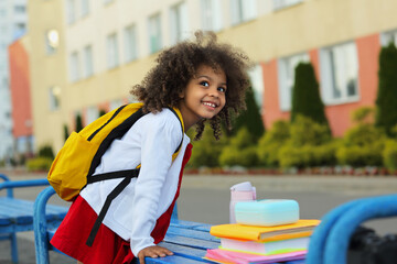 Cute Black schoolgirl eating lunch outdoors next the school. Healthy school breakfast for child.