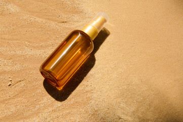 Unbranded dark glass bottle with SPF oil or sunscreen body lotion on sand beach background. Summer cosmetic concept.