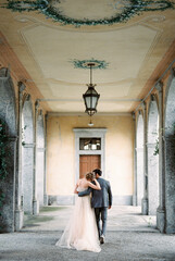 Fototapeta na wymiar Bride and groom walk hugging along the terrace of an old villa. Back view