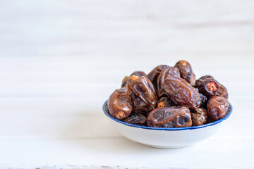 Dried date fruits in traditional bowl on white wooden background with copy space.