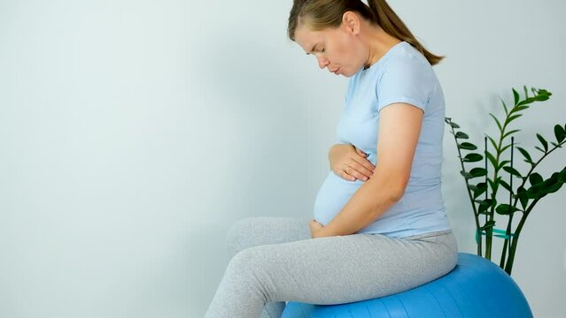 Pregnant woman feels contractions sitting on fitball and do breathing exercise to relief pain from labors. Pregnancy and childbirth.