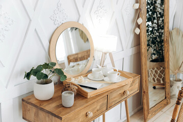 Wooden boudoir table with vintage chair. Full length mirror with wooden frame. Flowers in pots indoors. Wooden floor. Scandinavian style handmade wooden furniture. Boho style interior. Nobody