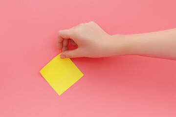 Woman's hand glues yellow sticker or sticky notes on pink background.