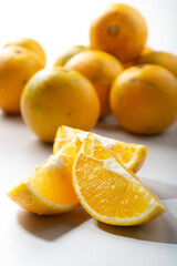 three pieces of yellow oranges for juicing cut in front of a group of oranges on a white background
