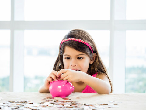 Happy little girl putting money in a piggy bank