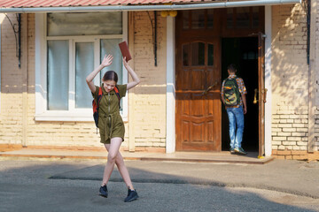 a teenage girl, being a student, is having fun near the entrance to the school building, waving her...