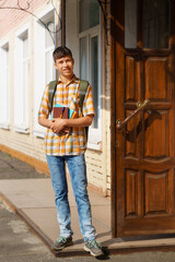 a portrait of a teenage boy, a student, stands next to the entrance to the school building