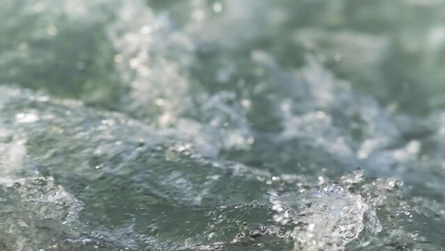 Sun shines on rapid river water, closeup abstract detail, slow motion video