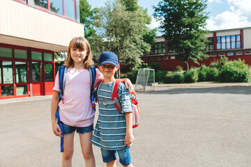 Portrait of a boy and a girl with backpacks on their backs in the school yard. Schoolchildren...