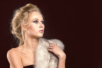 Cute blonde girl with fur over her looking to the side on a black background in the studio.
