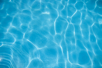 ripples of water from a swimming pool with a blue background with the sun reflecting in the water