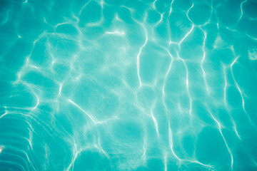 ripples of water from a swimming pool with a blue background with the sun reflecting in the water