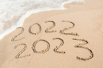 Inscription 2022 and 2023 numbers written on sand.  New Year 2023 replace 2022. Concept on the sea beach