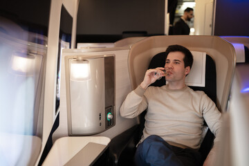 Young rich man on board of first class drinking champagne, enjoying financial success.
