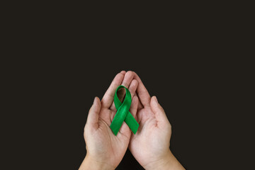 Adult hands holds green ribbon on black background. World lymphoma awareness day. September 15. Liver, Gallbladders bile duct, kidney Cancer and Lymphoma Awareness month.