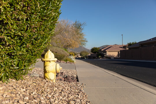 Yellow fire hydrant on bed of pebbles next to a sidewalk in suburban neighborhood