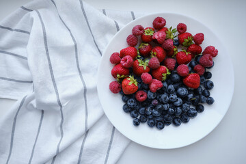 Plate with delicious raspberry strawberries and blueberries on a light background. 