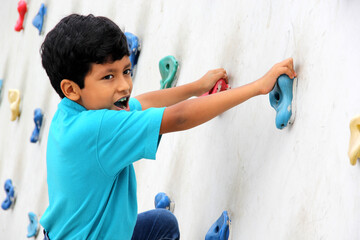 Latin dark-haired male child with blue t-shirt practicing sports wall climbing without fear of...