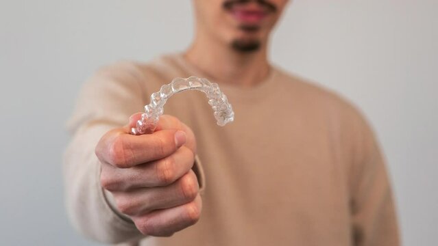 Caucasian young man showing an invisible silicone aligner for dental correction. Male hand holding the plastic braces dentistry retainers to straighten teeth
