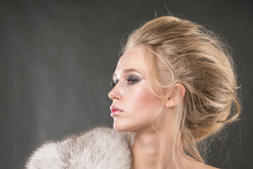 Beautiful blonde with draped fur in profile on a gray background. Close-up.