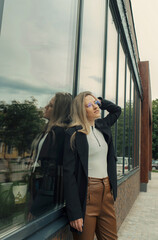 A beautiful woman stands leaning against the window of a building, touches her hair with her hands.