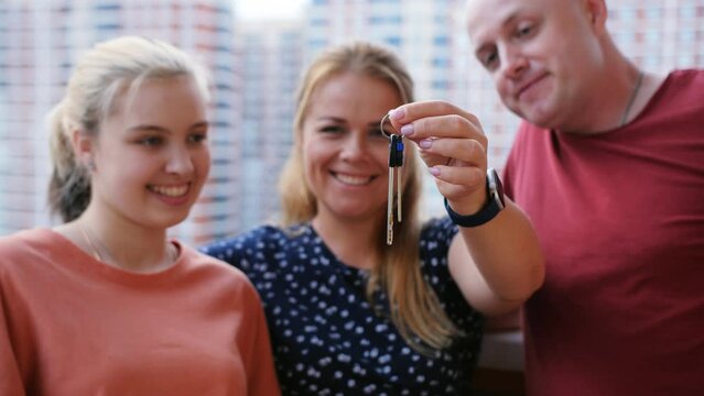 A woman with her daughter and husband on the balcony of a new apartment shakes her keys looking at the camera.