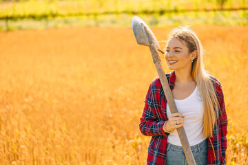 Smiling girl farmer holding a shovel to inspect a beautiful field during warm light organic farming...