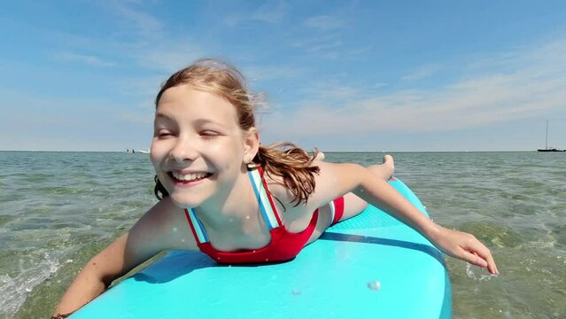 Happy girl having fun swimming on surfboard in sea during summer family vacation