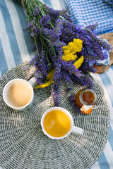 summer bouquet of yellow yarrow and violet lavender, 2 cups of tea with milk and jar of tangerine jam on a striped picnic blanket with summer vibe - 520679348