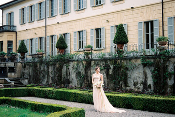 Bride stands on a gravel path in the park near the old villa. Como, Italy