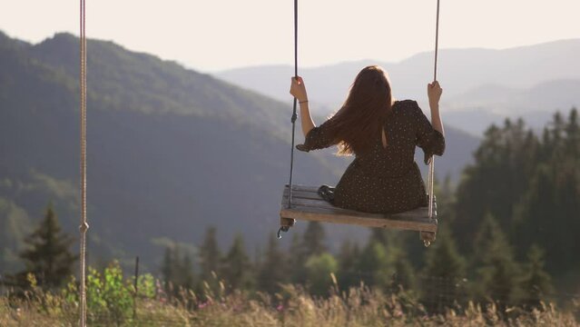 Single young woman in a rope wooden swing over the breathtaking mountain panorama