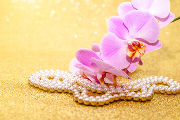 purple Orchid and pearl necklace on a shiny gold background
