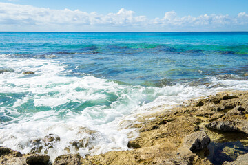 Sea waves crash against the coastal reefs. Turquoise sea, rocky coast on a sunny day. Landscape