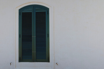 Fototapeta premium A window in an old building with green shutters. Green closed shutters. Minorca, Spain