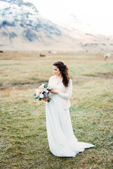 Fototapeta na wymiar Bride in a white dress with a bouquet on a green pasture. Iceland