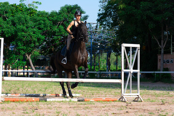 young girl jockey is training, jumping over the barrier on a dark-colored horse. Dressage and show...