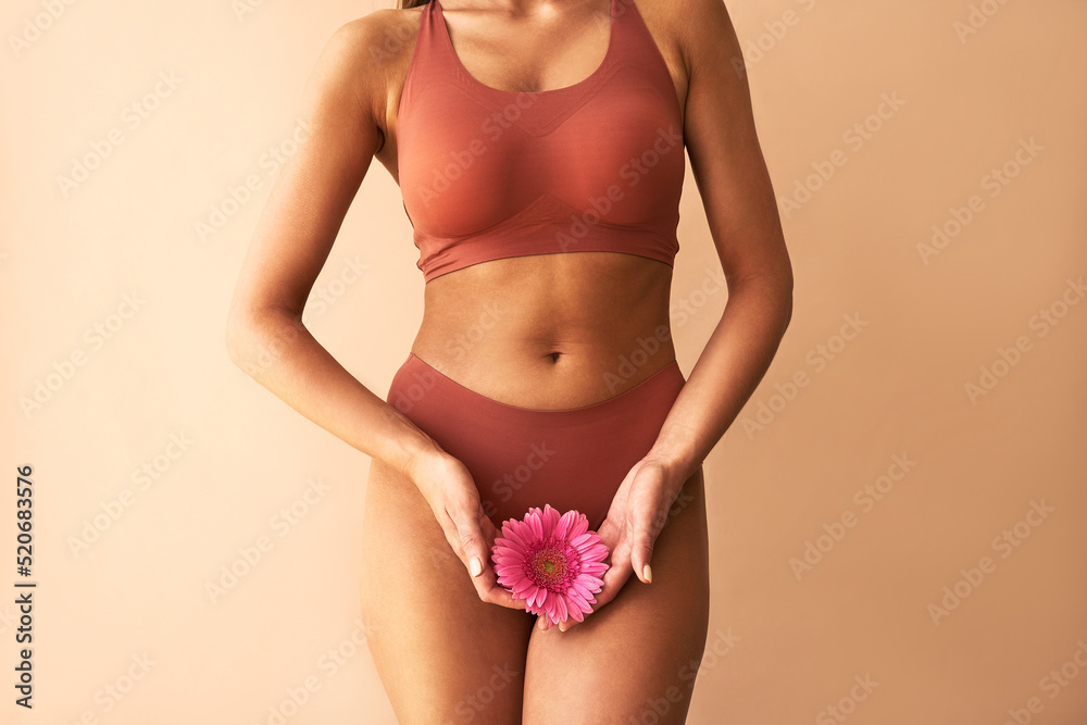 Wall mural Cropped image of woman in lingerie holding pink flower on beige background. Women's health, cosmetology.