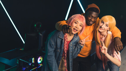 Teenage gamers in colorful clothes posing for photo in front of professional gaming setup smiling...