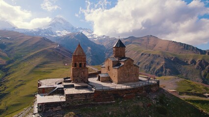 amazing aerial view of Gergeti Trinity Church surrounded by the Caucasus mountains in the sunny weather, Kazbegi, Georgia. High quality photo