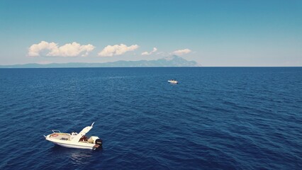 Bird's eye perspective of a seascape. Calm dark-blue sea waters, two white private small boats - one in the foreground, one in the background. Mountain island on the horizon. High quality photo - obrazy, fototapety, plakaty