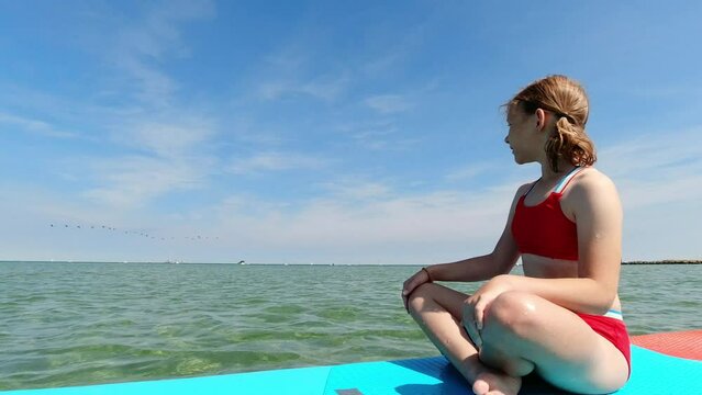 Teenage girl sitting and thinking on sup board in sea at summer holidays