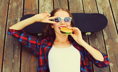 Portrait of happy smiling young woman with burger and skateboard wearing sunglasses on city street background © rohappy