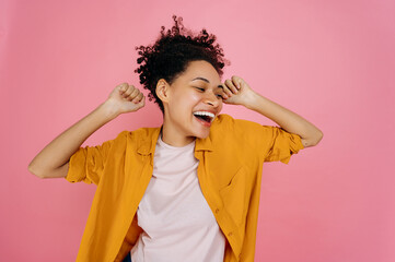 Happy cheerful african american girl in casual wear, dancing to favorite music, having fun, rejoice in luck, celebrating win, smiling, stand on isolated pink background. Joy, victory, luck, dancing