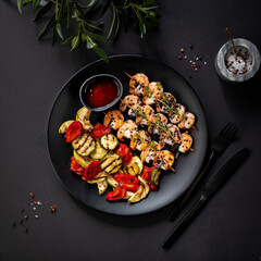 shrimp kebab with sauce and grilled vegetables on a black plate on a black background
