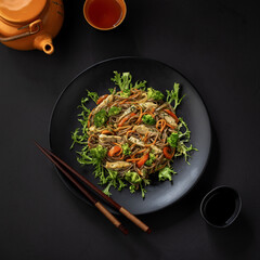 Mix the fried noodles with vegetables and meet in a black bowl. Slate background. View from above.